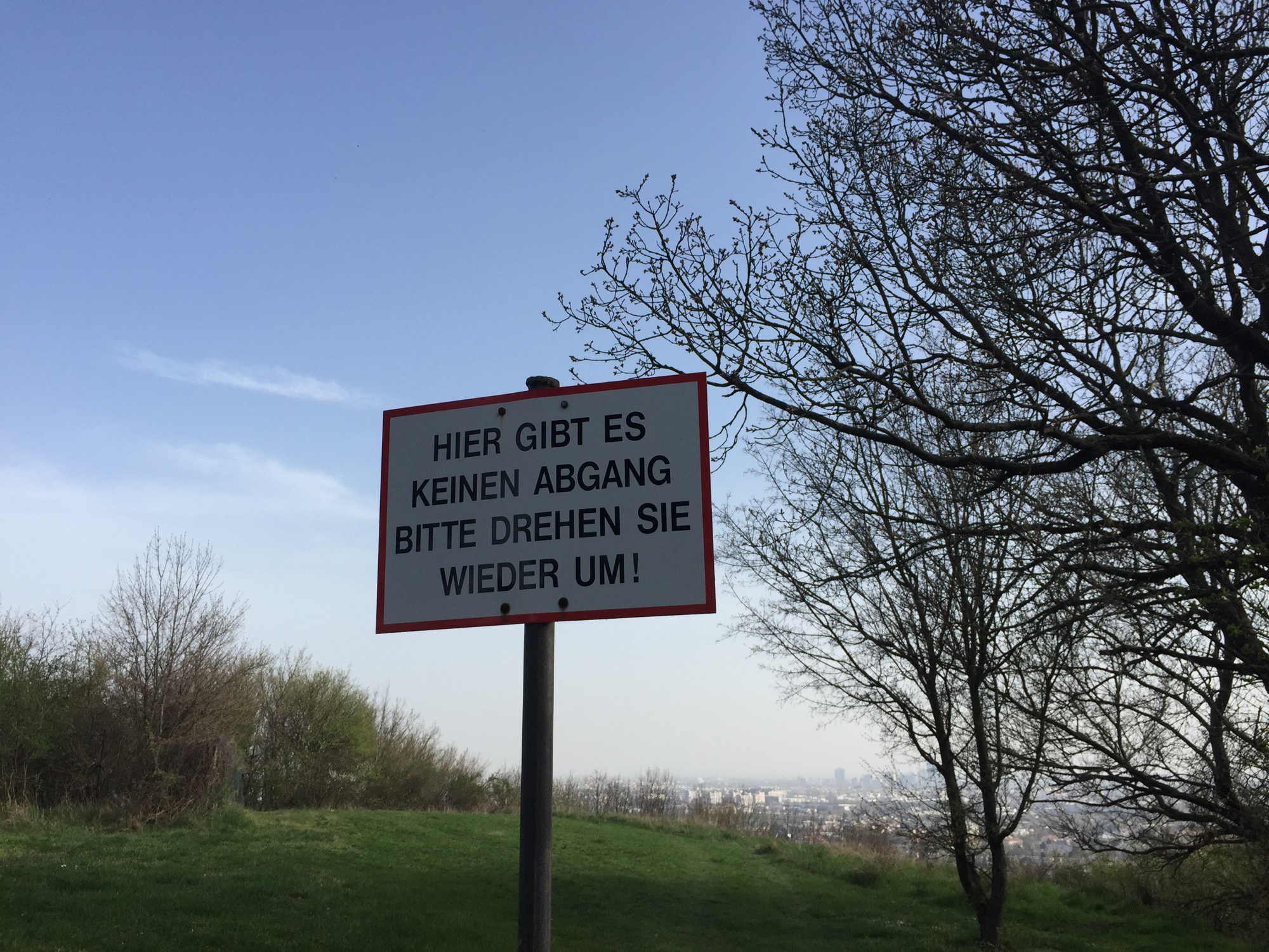 Schild: Hier gibt es keinen Abgang. Bitte drehen Sie wieder um. Hintergrund: Blick auf Wien