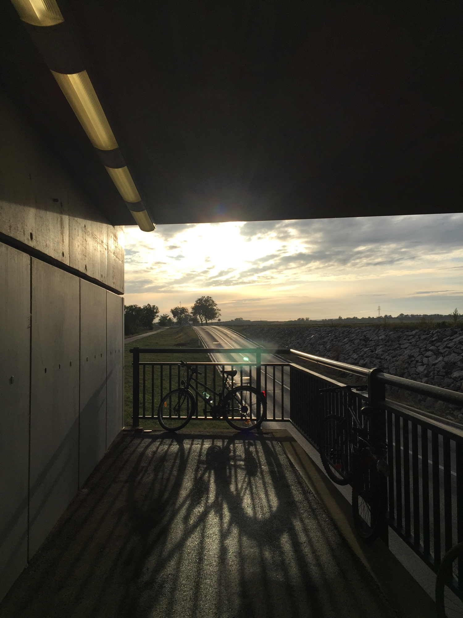 Unterführung am Bahnhof Obersdorf, Sonne durchbricht Wolken, im Vordergrund ein Fahrrad am Geländer, das lange Schatten wirft