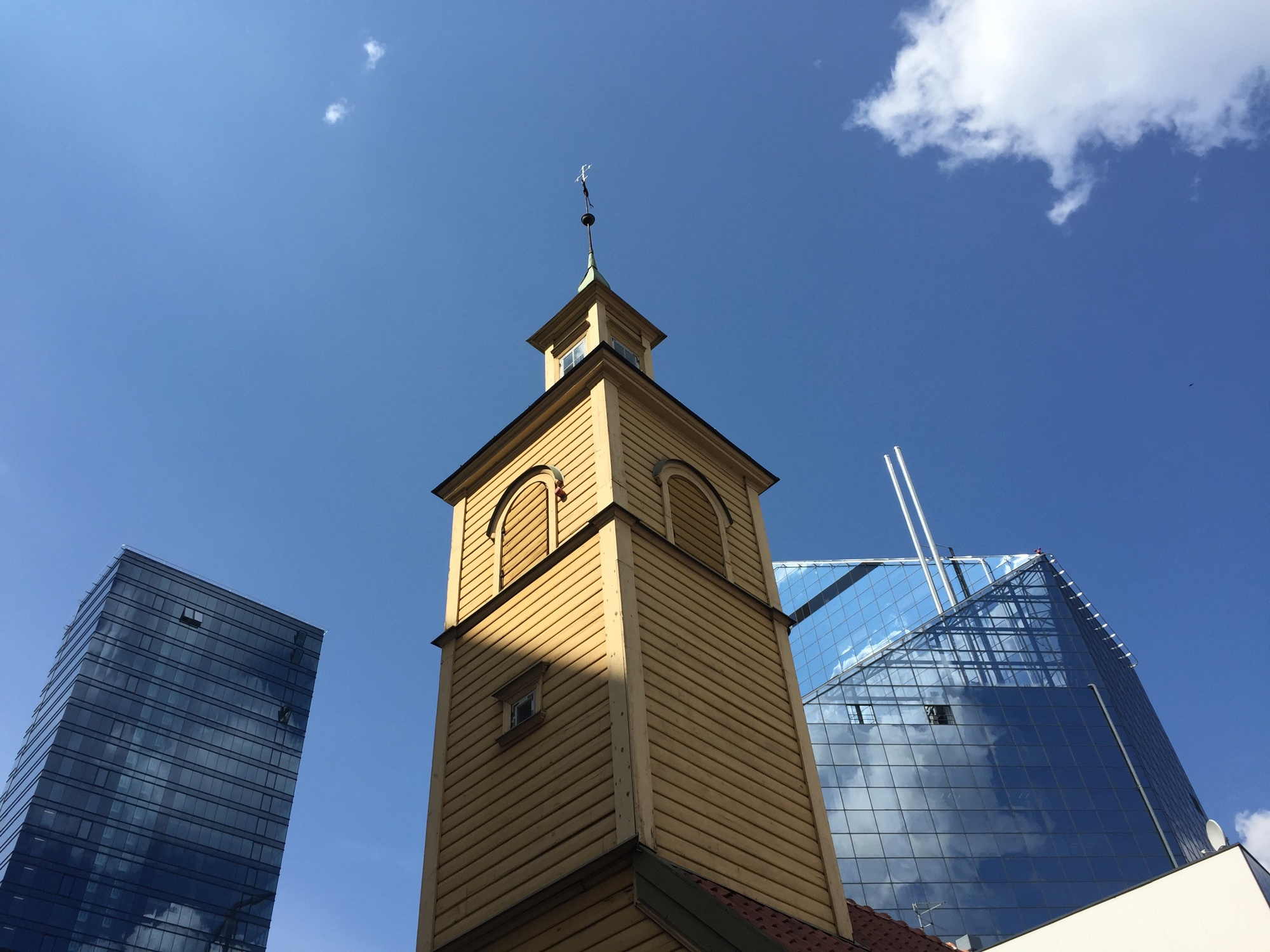 Kontrast zwischen alten Gebäuden und neuen Glaspalästen im Stadtzentrum von Tallinn: altmodischer Holzkirchturm vor glasverkleideten Wolkenkratzern