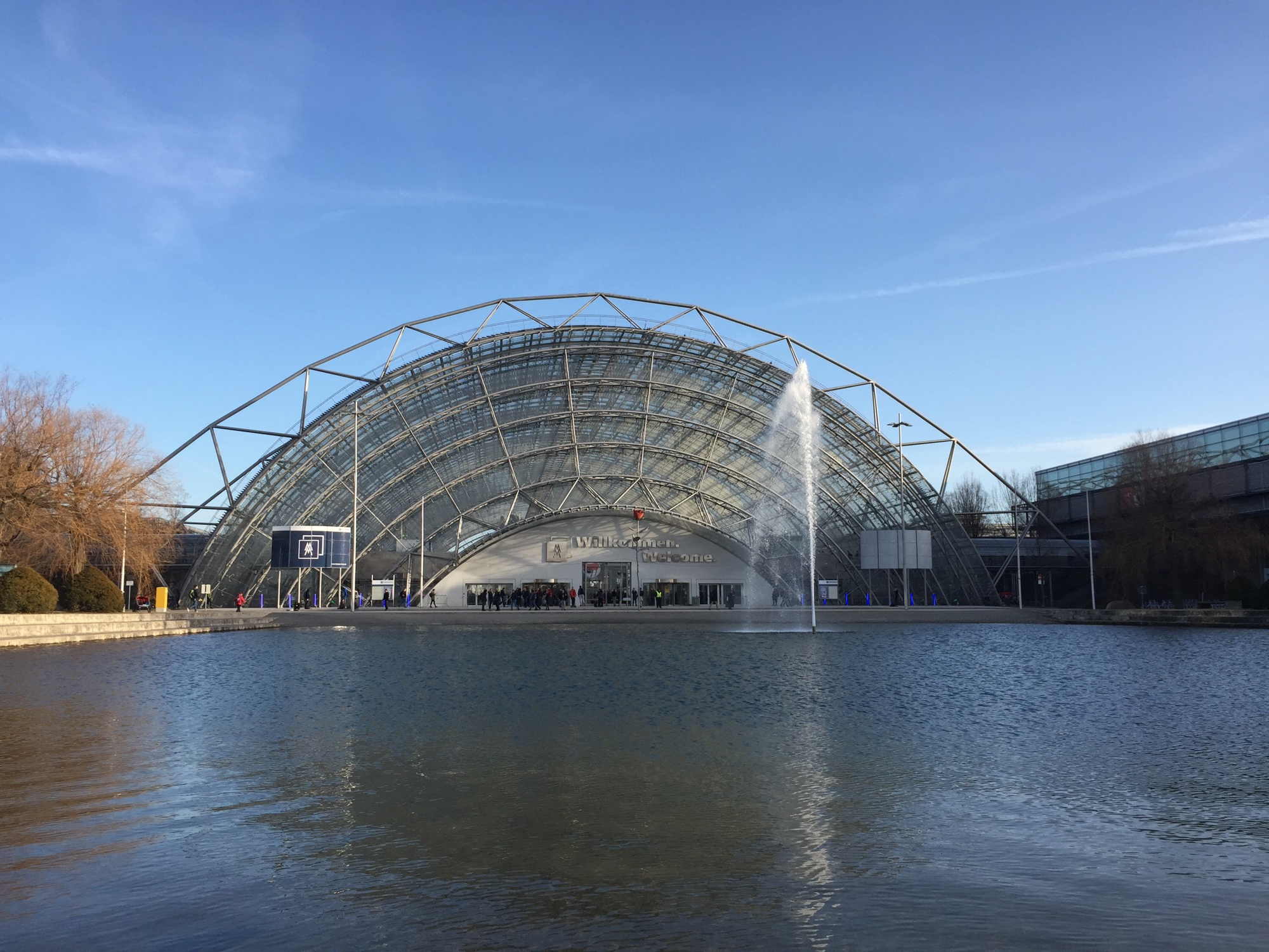 Glashalle der Leipziger Messe von außen, mit Brunnen im Vordergrund, ein sonniger Tag