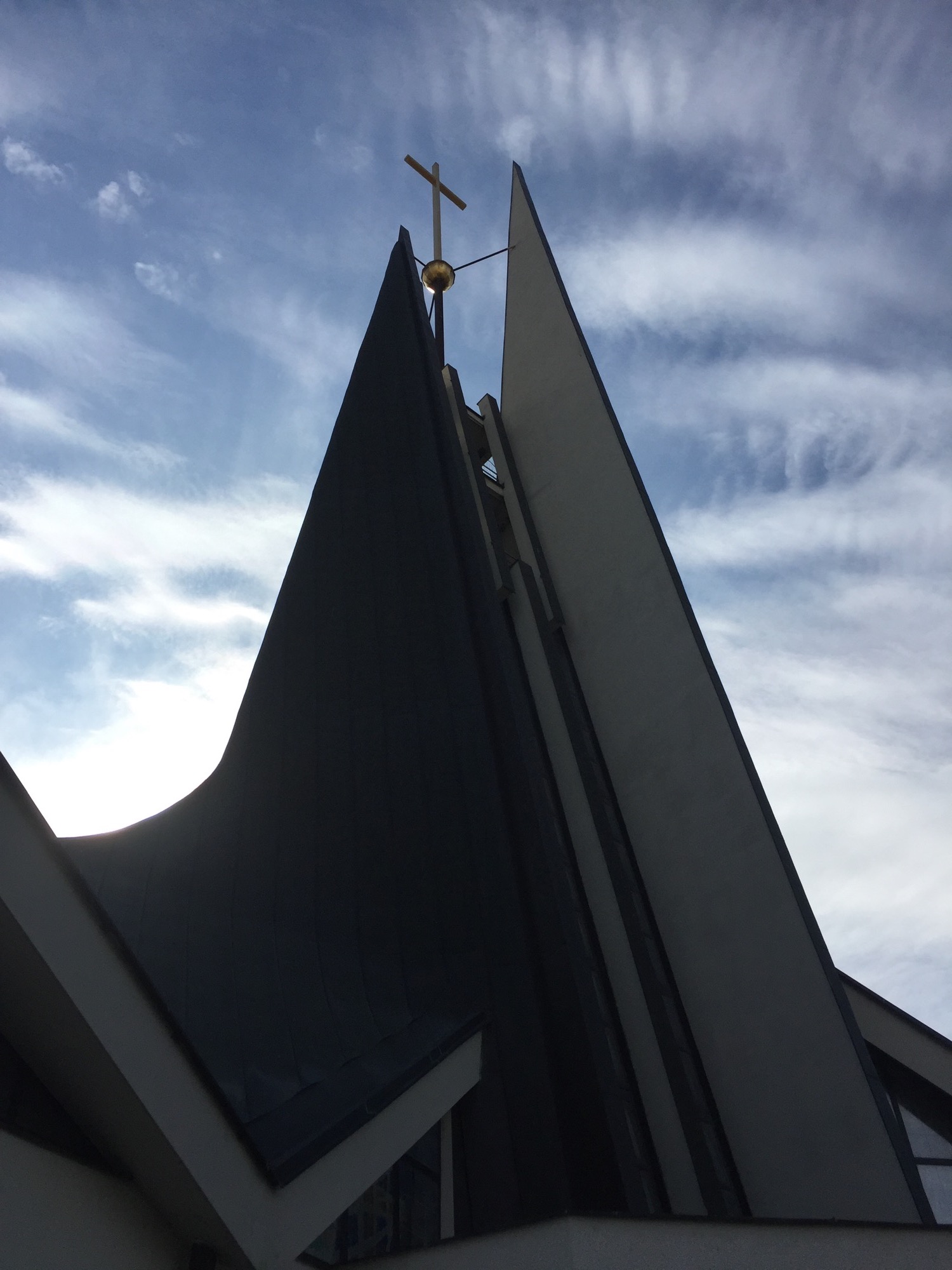 modernes Kirchengebäude St. Wenzel, Rückansicht, der Turm als Silhouette vor leicht bewölktem Himmel