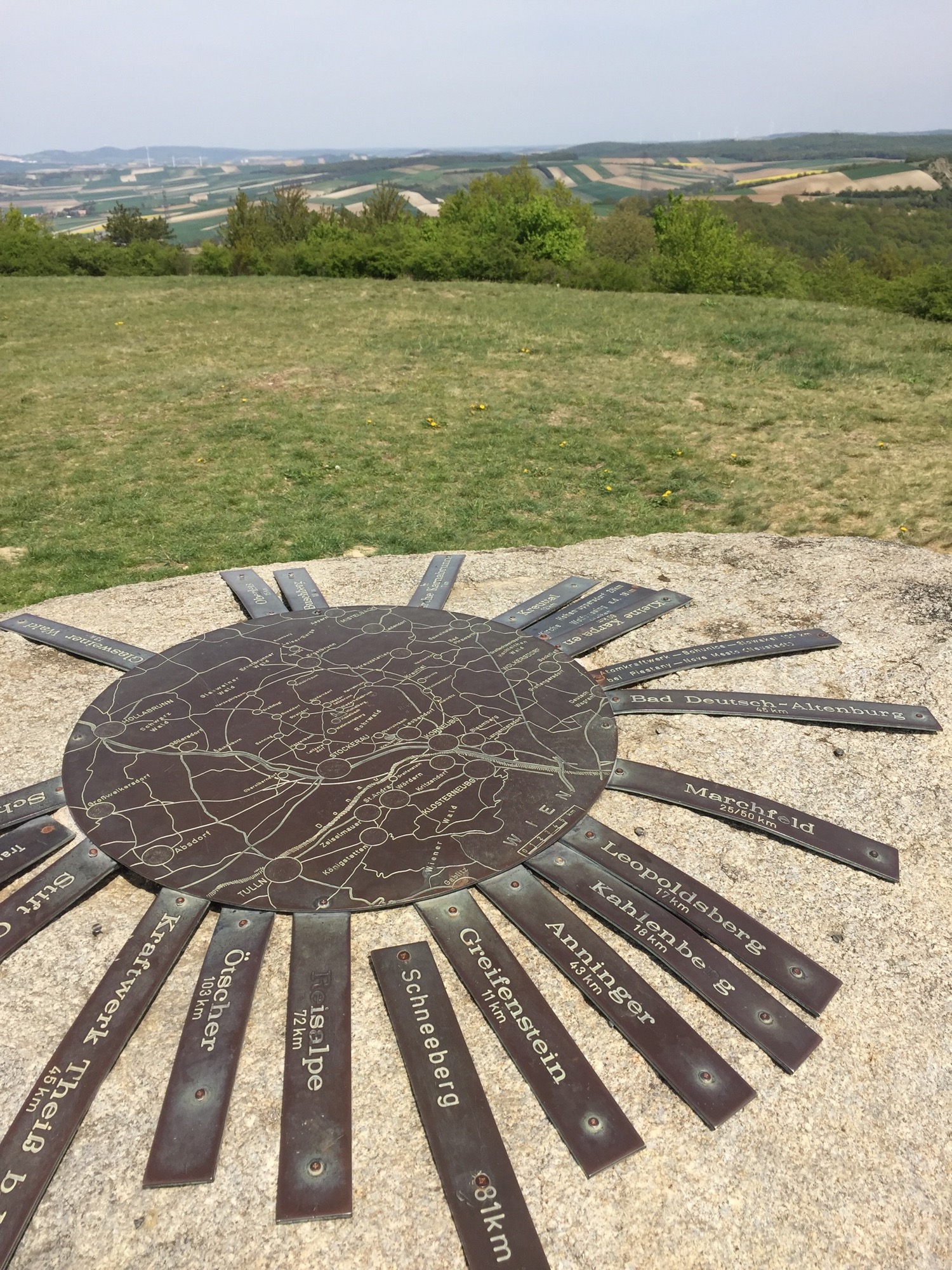 runde Metallplatte mit einer Karte der Region auf einem Stein, Richtungen und Entfernungen von anderen Destinationen gehen wie Strahlen von der Metallplatte aus in die jeweiligen Richtungen