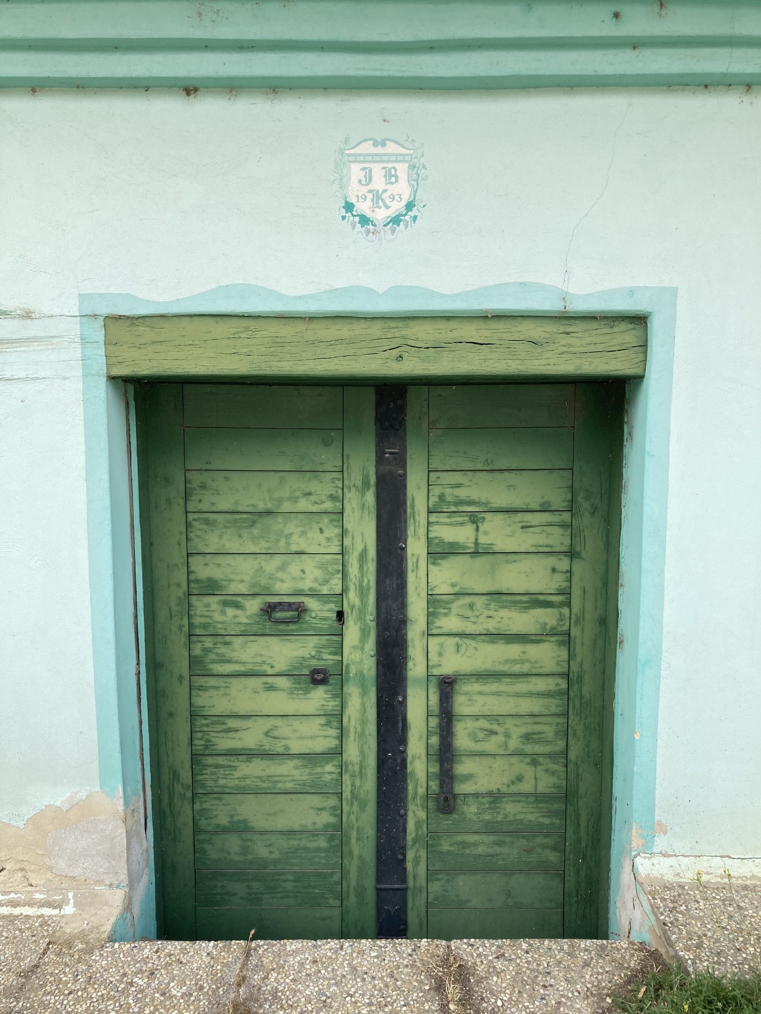 grünes zweiflügliges Tor als Kellerzugang, über dem Tor ein Wappen mit den Buchstaben JBK und der Jahreszahl 1993