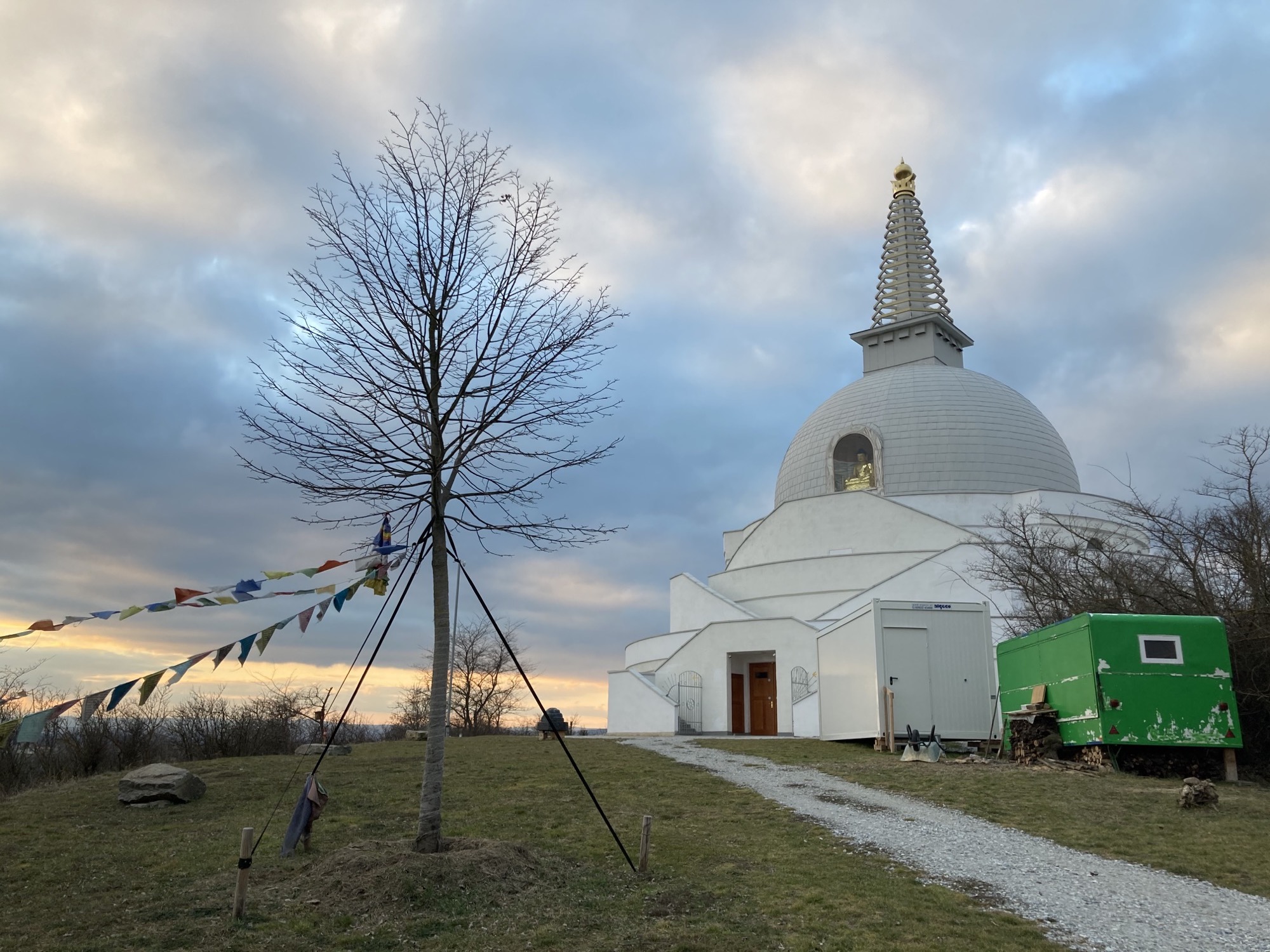 buddhistische Friedensstupa, weiß mit goldener Spitze, im Vordergrund ein Baum mit buddhistischen Gebetsflaggen