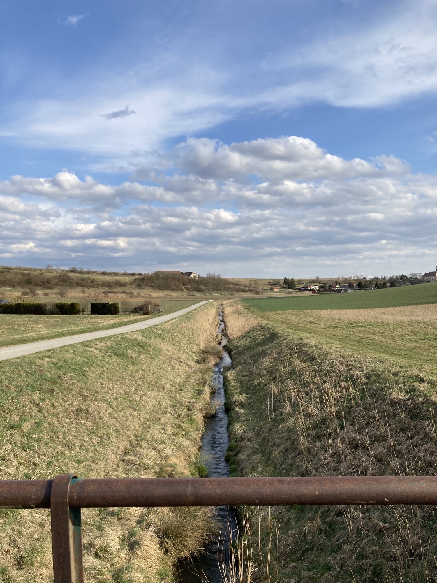 Ausblick von der Brücke über den Weidenbach, im Hintergrund leicht bewölkter blauer Himmel