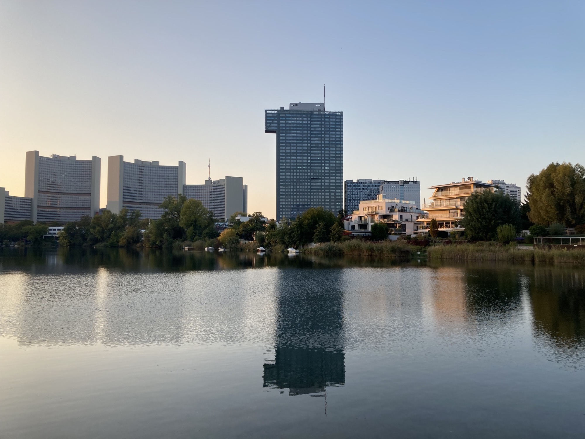 Blick über einen Nebenarm der Alten Donau, links im Bild das Vienna International Center, in der Mitte ein Hochhaus, das sich im Wasser spiegelt