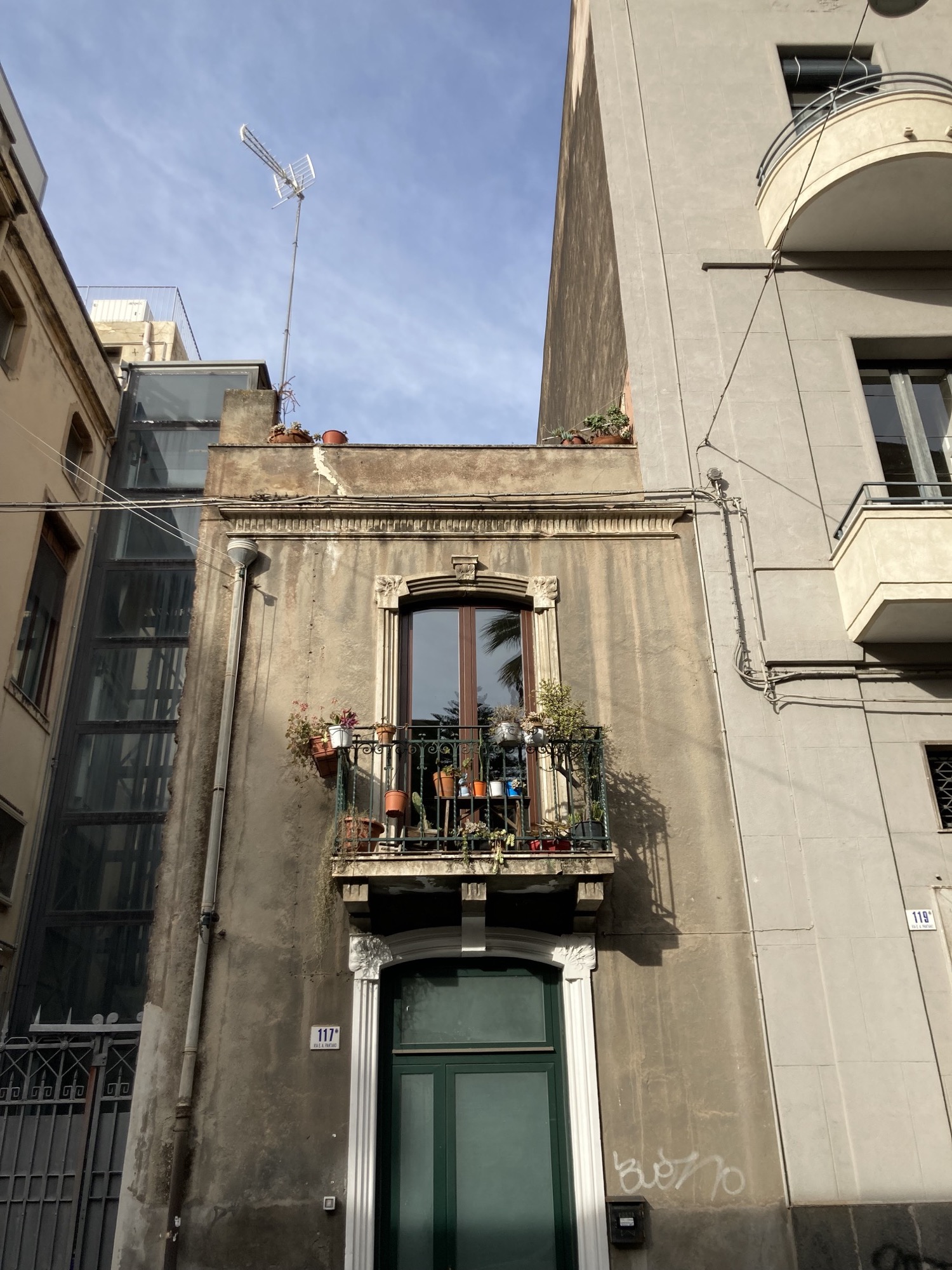 schmales Haus mit typischem sizilianischem Stil: hohes Fenster, davor ein sehr schmaler Balkon mit vielen Blumentöpfen