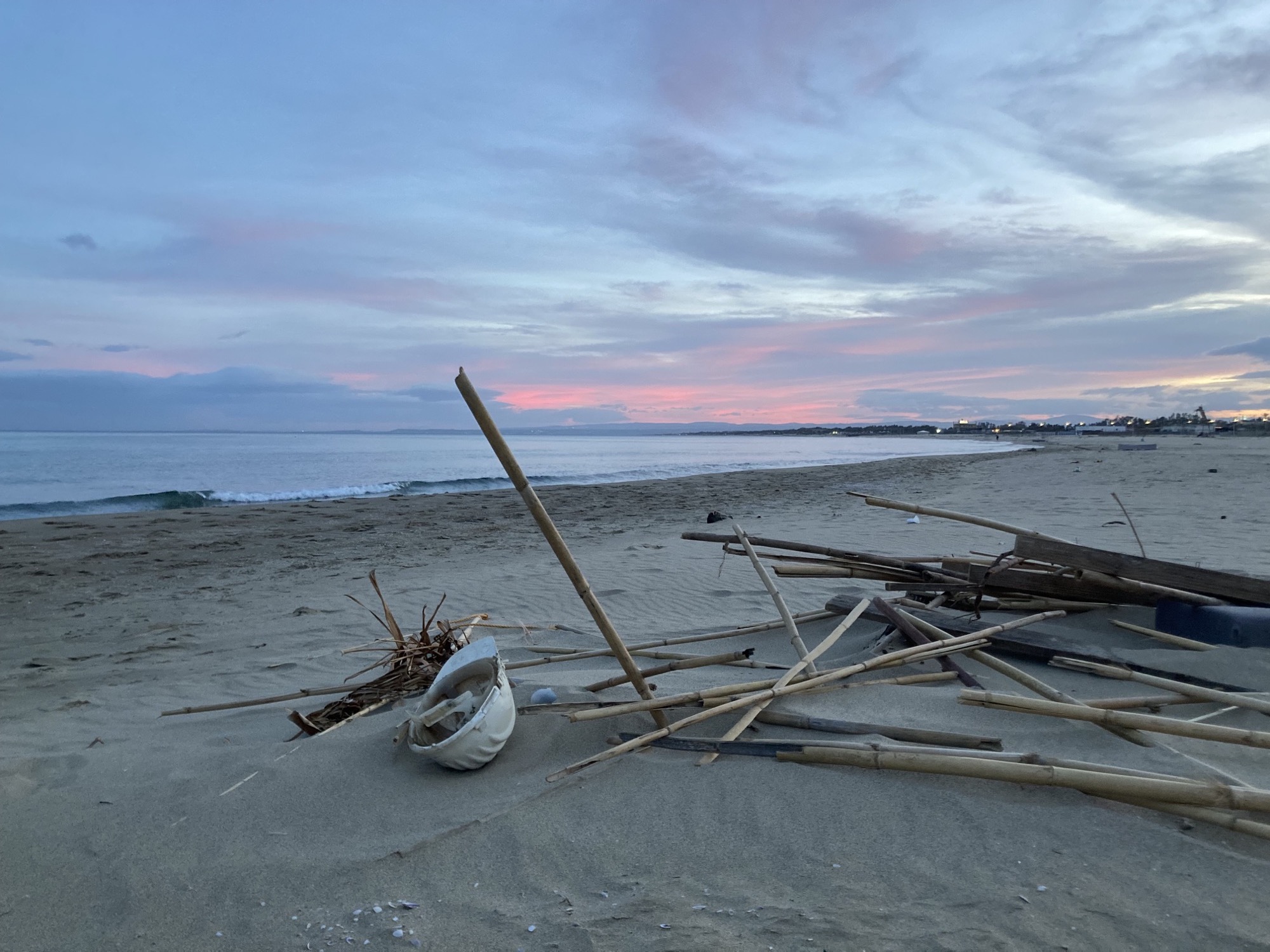 Strand von Catania im Abendlicht, im Vordergrund etwas Treibgut: Holz, Bambusstäbe, ein weißer Baustellen-Schutzhelm