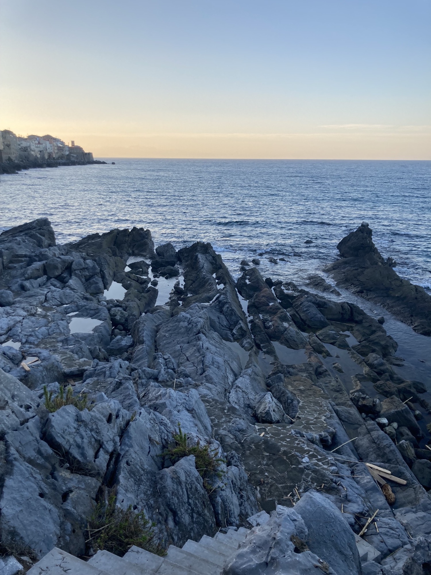 Küstenweg in Cefalú, leicht befestigte Felslandschaft an der Küste, Sonnenuntergang im Hintergrund
