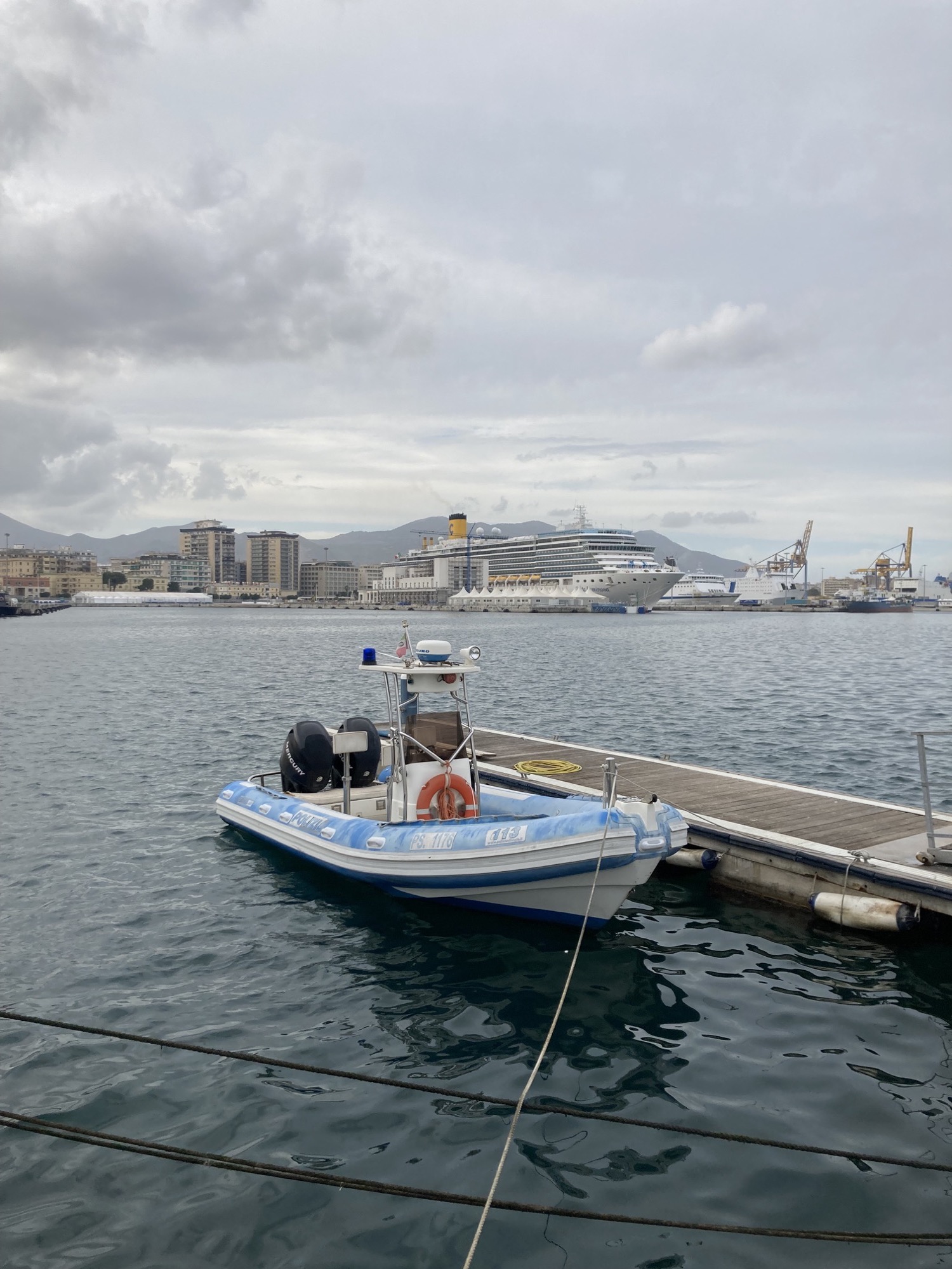Motorboot an einem kleinen Steg, im Hintergrund ein gigantisches Kreuzfahrtschiff