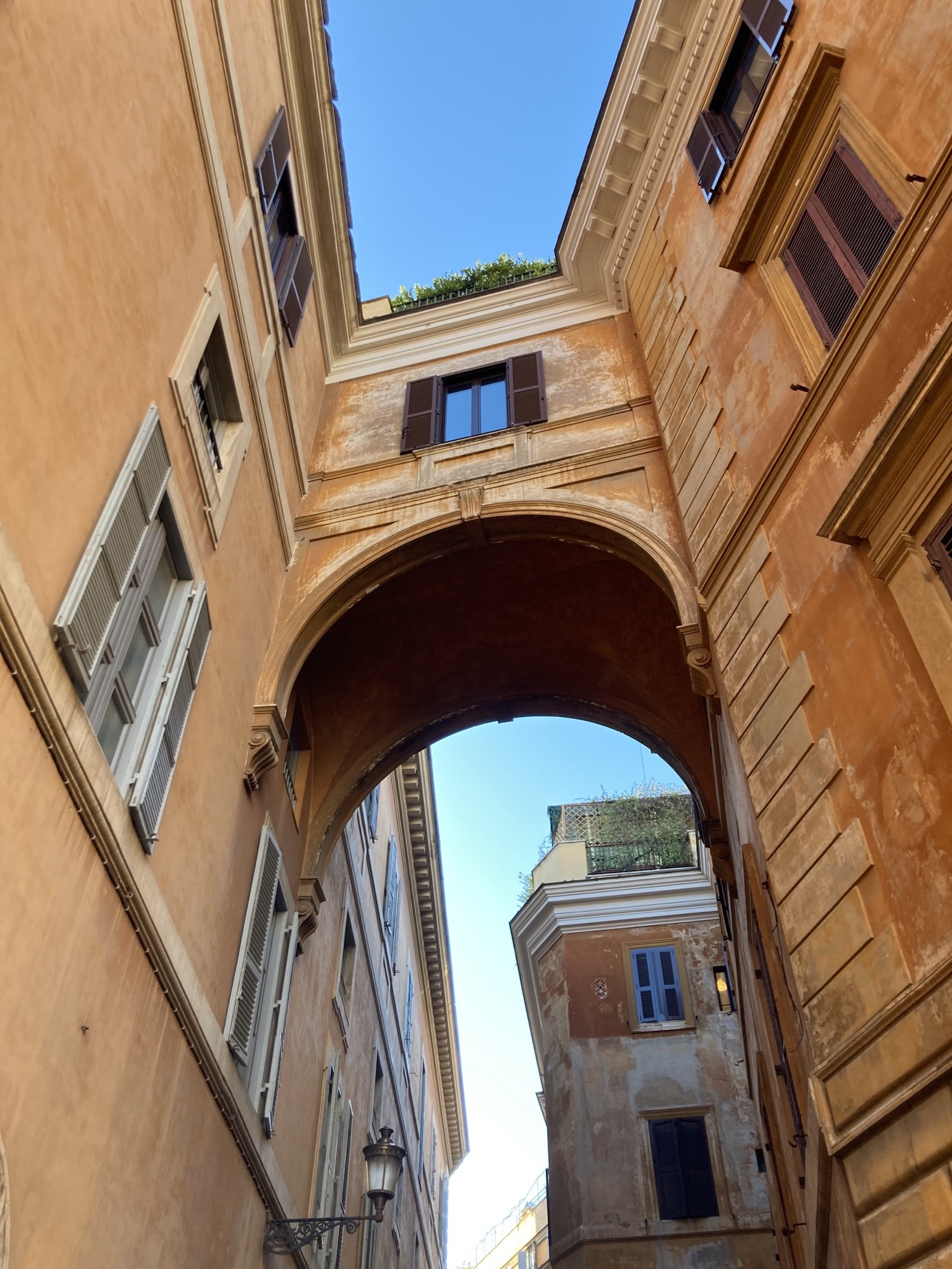 enge Gasse in Rom mit einem Verbindungsteil zwischen zwei Häusern in Gelbtönen, mit grünem Bewuchs auf dem Dach