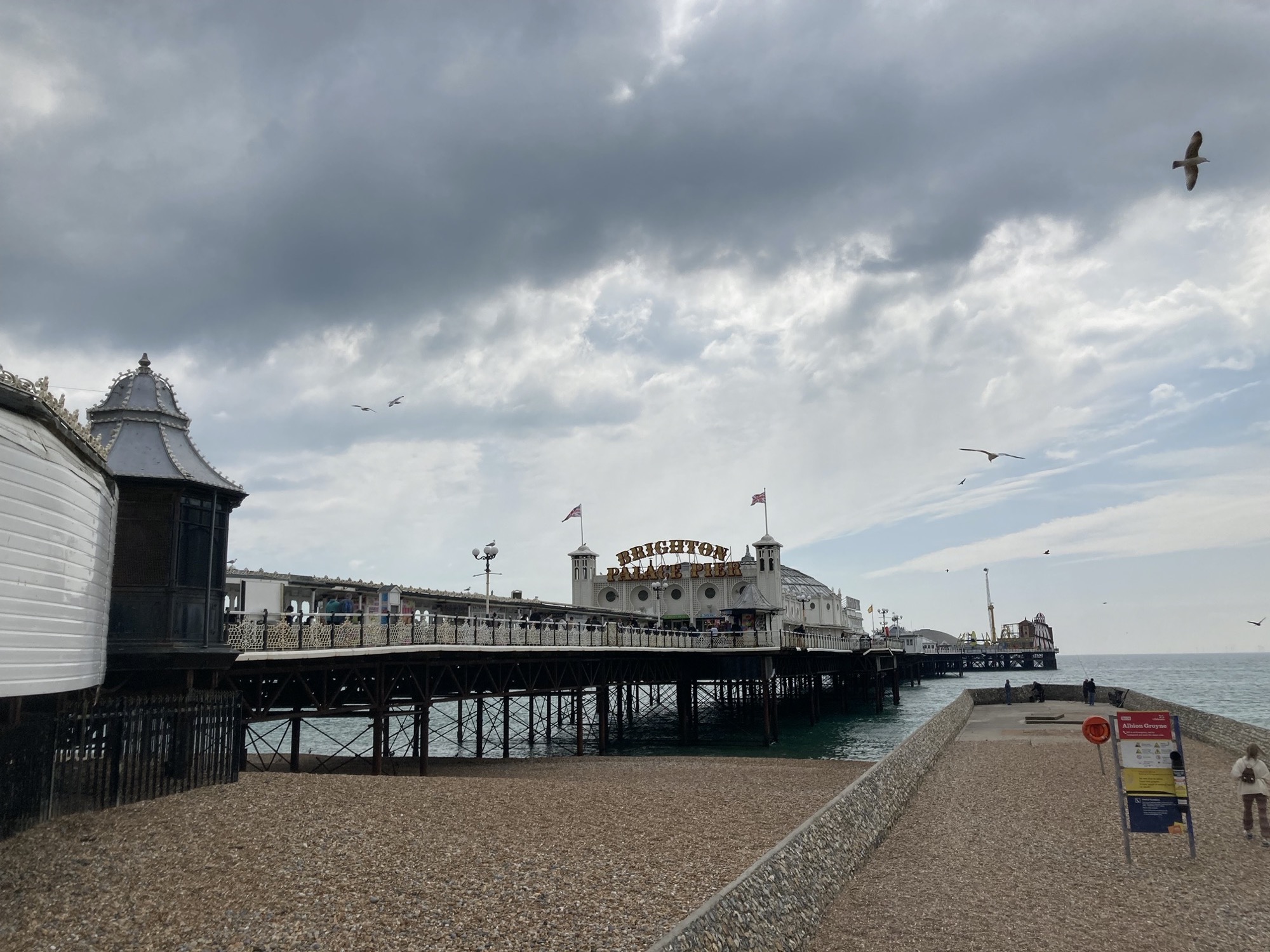Seebrücke Brighton Palace Pier ragt vom Strand aus gesehen ins Meer hinaus, im Mittelgrund die Spielhalle, rechts weiter hinten sind Teile der Gerätschaften des Vergnügungsparks zu sehen
