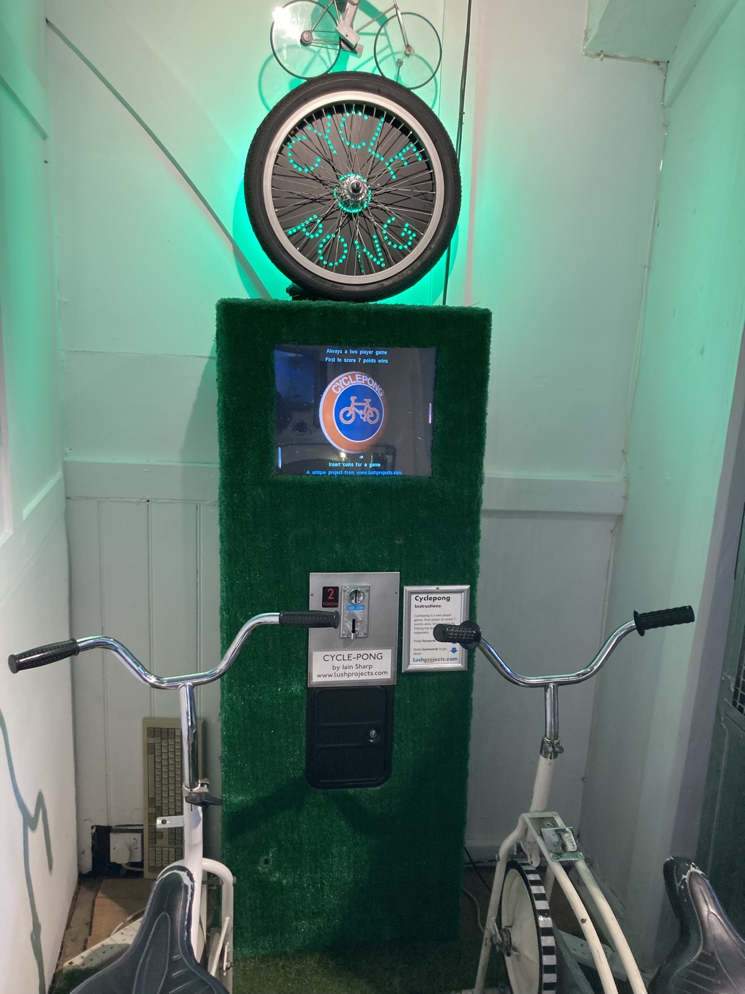 Cycle Pong, auf einem Bildschirm in der Mitte ist das bekannte Spiel Pong zu sehen, davor stehen zwei Fahrräder, mit denen die Nutzer:innen die Balken des Pong-Spiels nach oben und unten steuern können