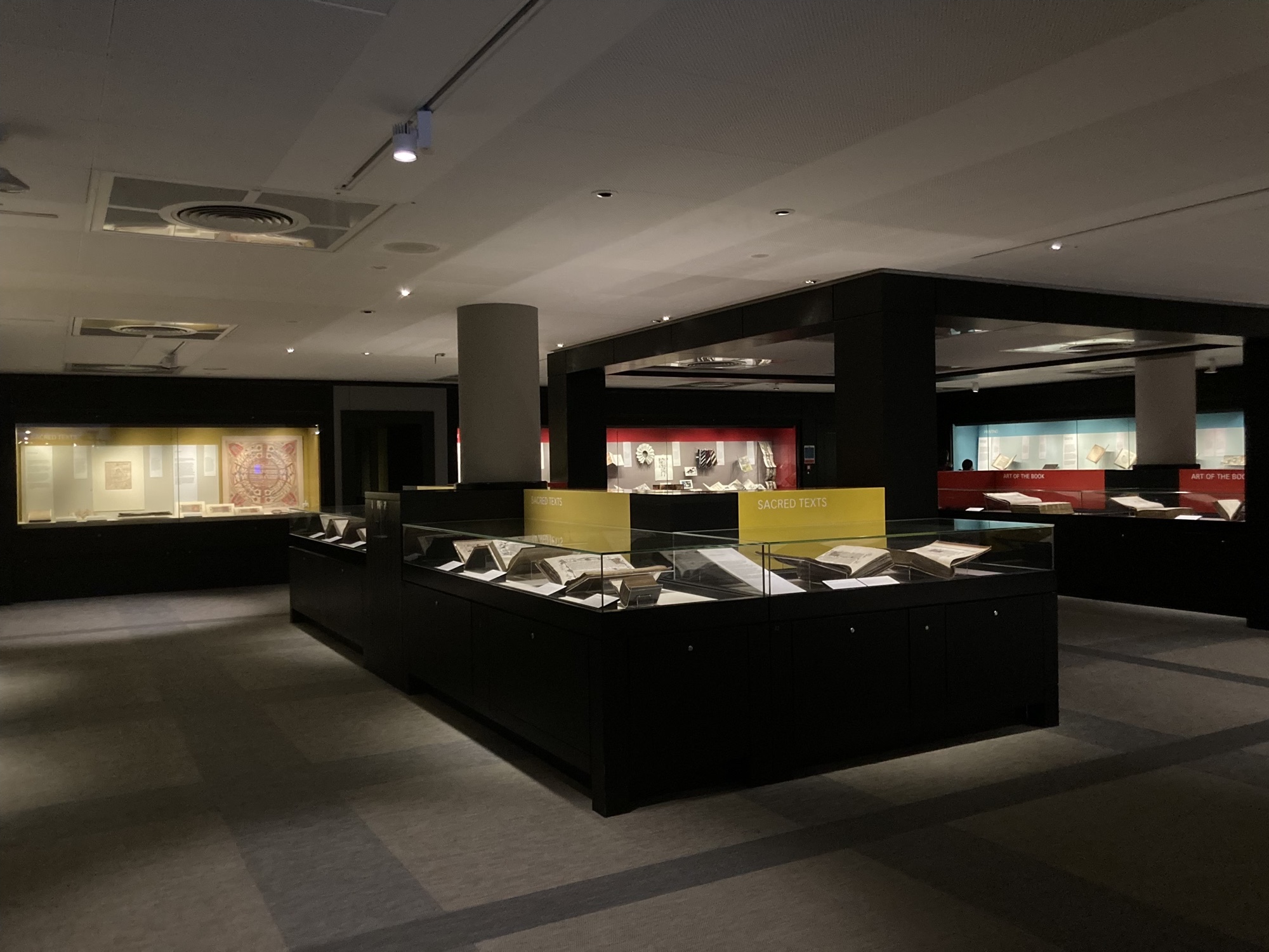 Blick in den Ausstellungsraum der Sir John Ritblat Gallery, gedämpftes Licht, schwarze Kästen, die mir Glas verkleidet sind, in diesen befinden sich wertvolle alte Bücher