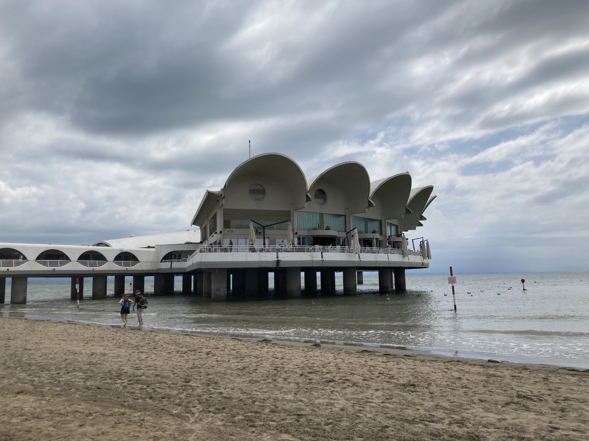 Terrazza a Mare, ein auf Pfeilern über dem Wasser errichtetes Gebäude mit einer Terrasse und Schirmen, das Dach besteht aus ausladenden muschelartigen Überhängen