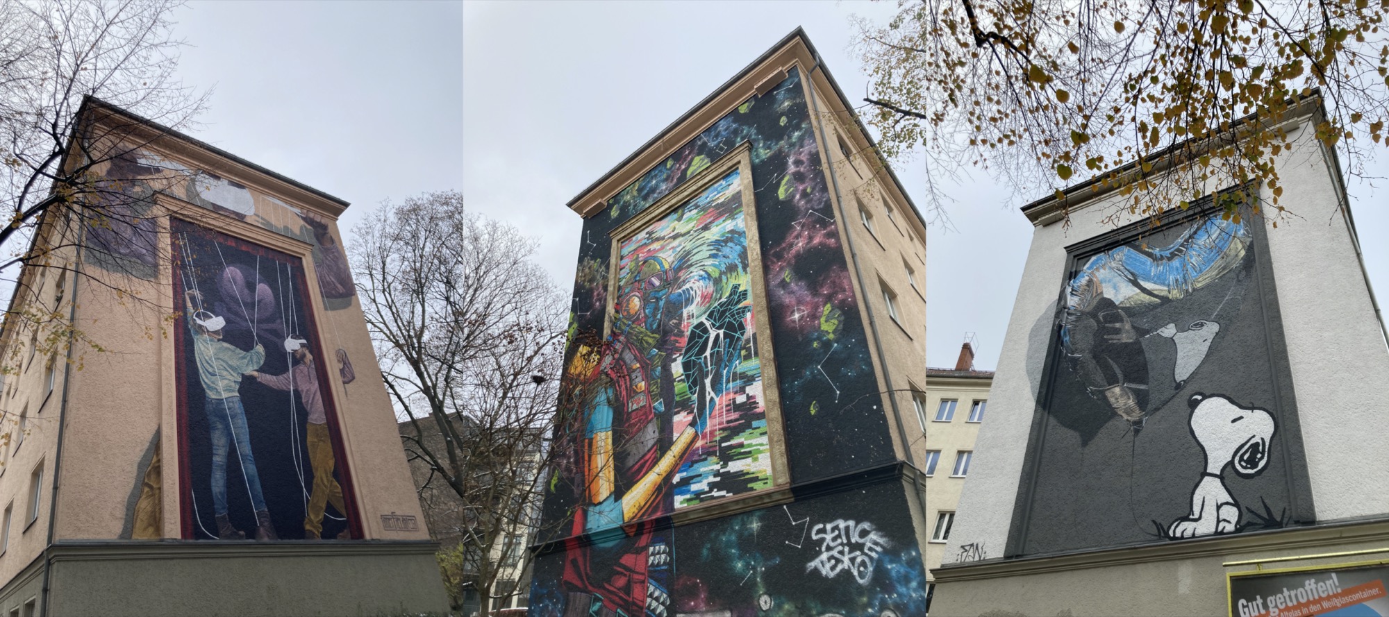 drei Graffiti an Hauswänden im Prenzlauer Berg, links: zwei Personen mit VR-Brillen, die an Marionettenschnüren von einer dritten Person darüber gesteuert werden, mitte: bunte Darstellung eines Roboters, der ein schwarzes Herz betrachtet, das aus einzelnen grafischen Teilen besteht, rechts: der Hund Snoopy betrachtet einen über ihm schwebenden herzförmigen Luftballon, in der Spiegelung auf dem Luftballon ist neben Snoopy ein sich umarmendes Paar angedeutet