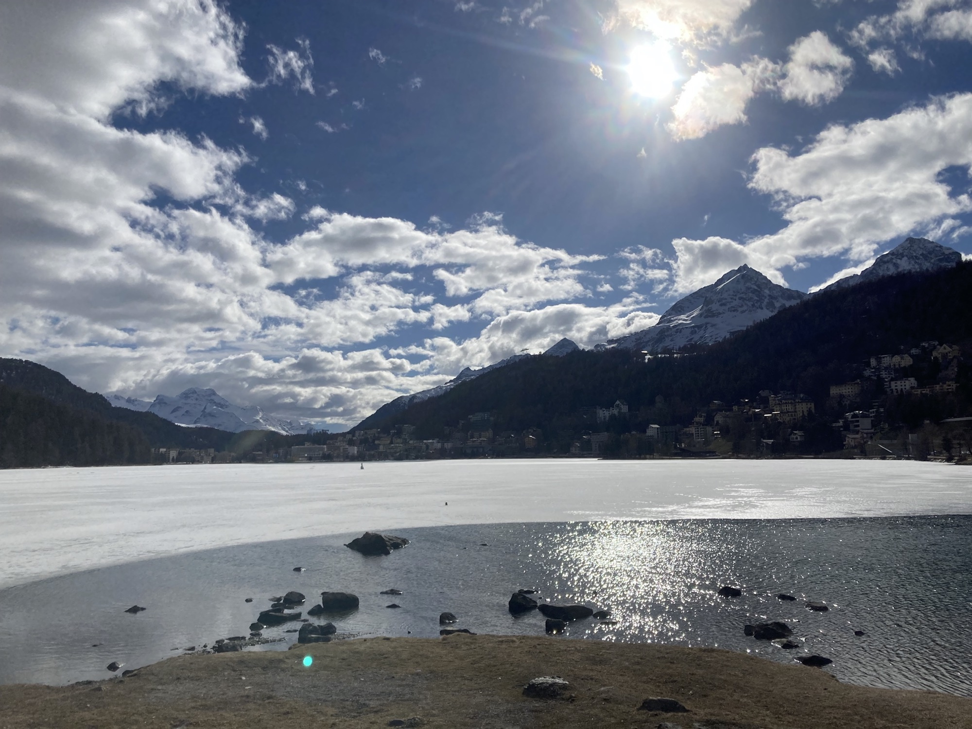 strahlender Sonnenschein über dem See von St. Moritz, am Rand ist die Eisfläche schon aufgetaut, der Großteil des Sees ist aber noch zugefroren
