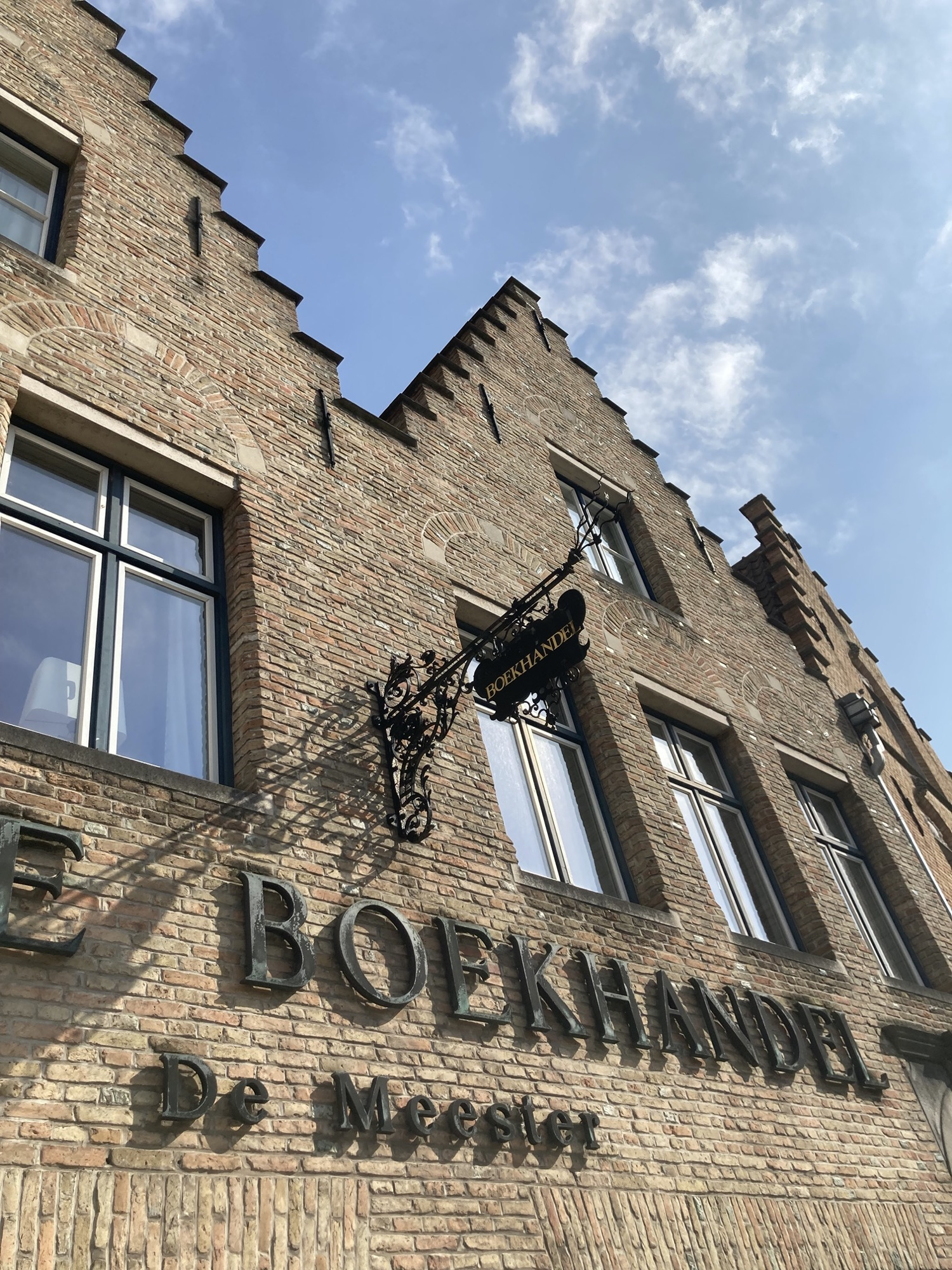 braunes Ziegelgebäude mit treppenförmigen Ziergiebeln, ein Wappen und eine Metallschrift auf dem Haus nennen den Namen „Boekhandel De Meester“