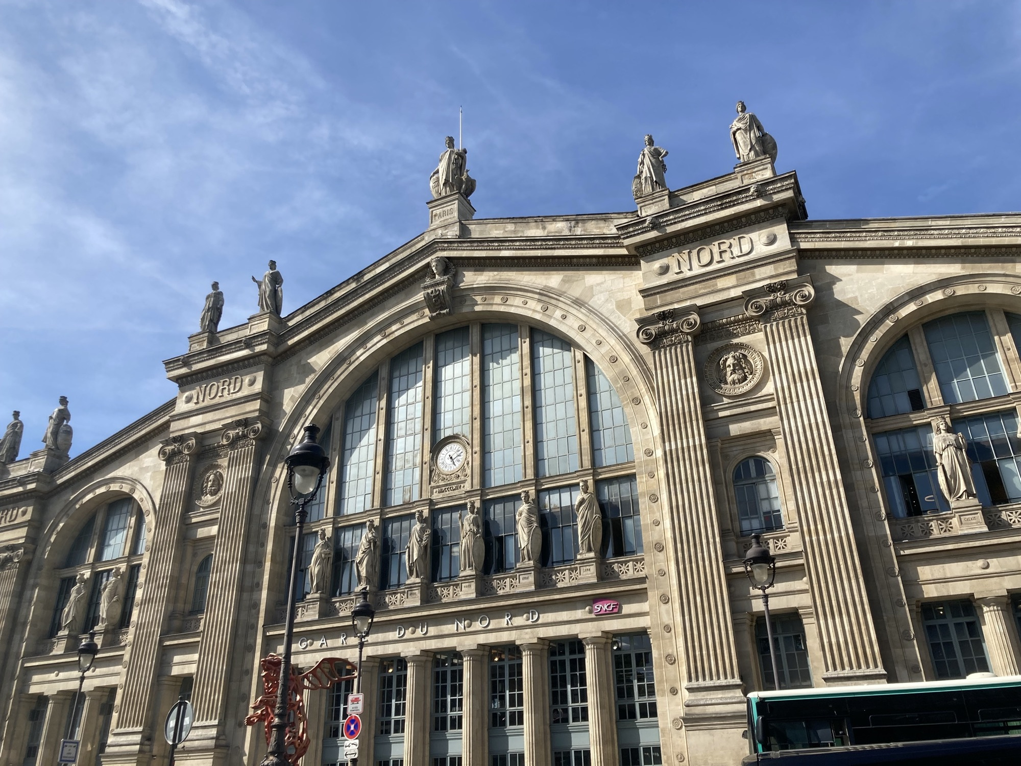 Bahnhofsgebäude des Gare du Nord, das Gebäude ist mit vielen Säulen und Statuen dekoriert und hat über dem Eingangsportal ein Glasfenster mit einer Uhr