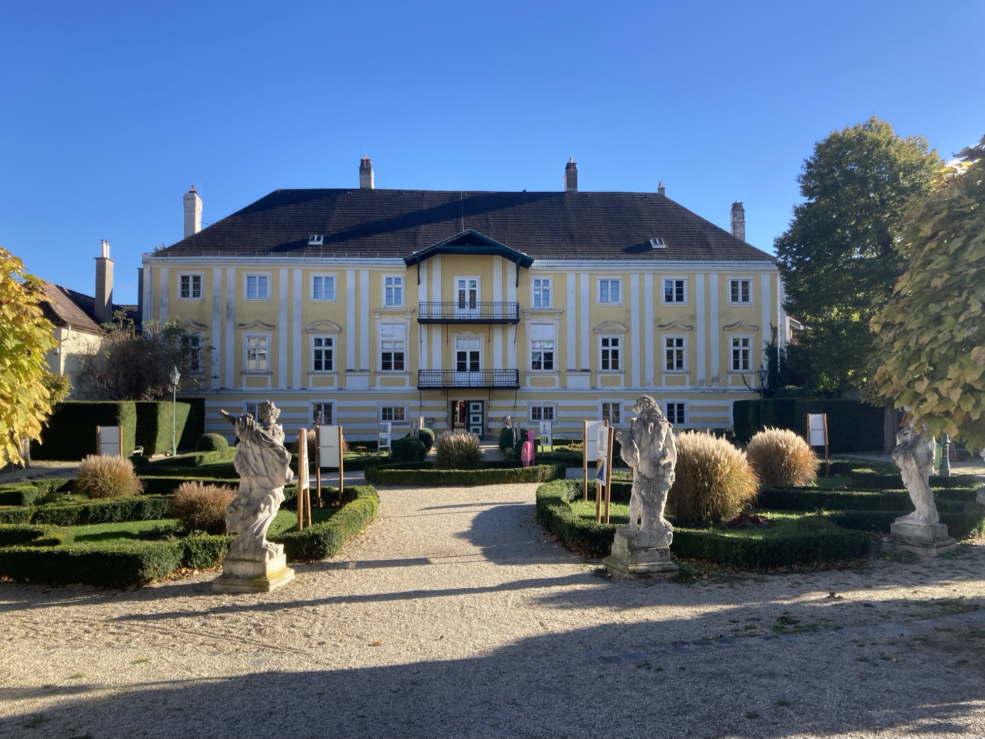 Knappenhof, ein imposantes gelb-weiß gestrichenes Gebäude, Nachmittagsherbstlicht fällt von rechts auf den Park vor dem Gebäude