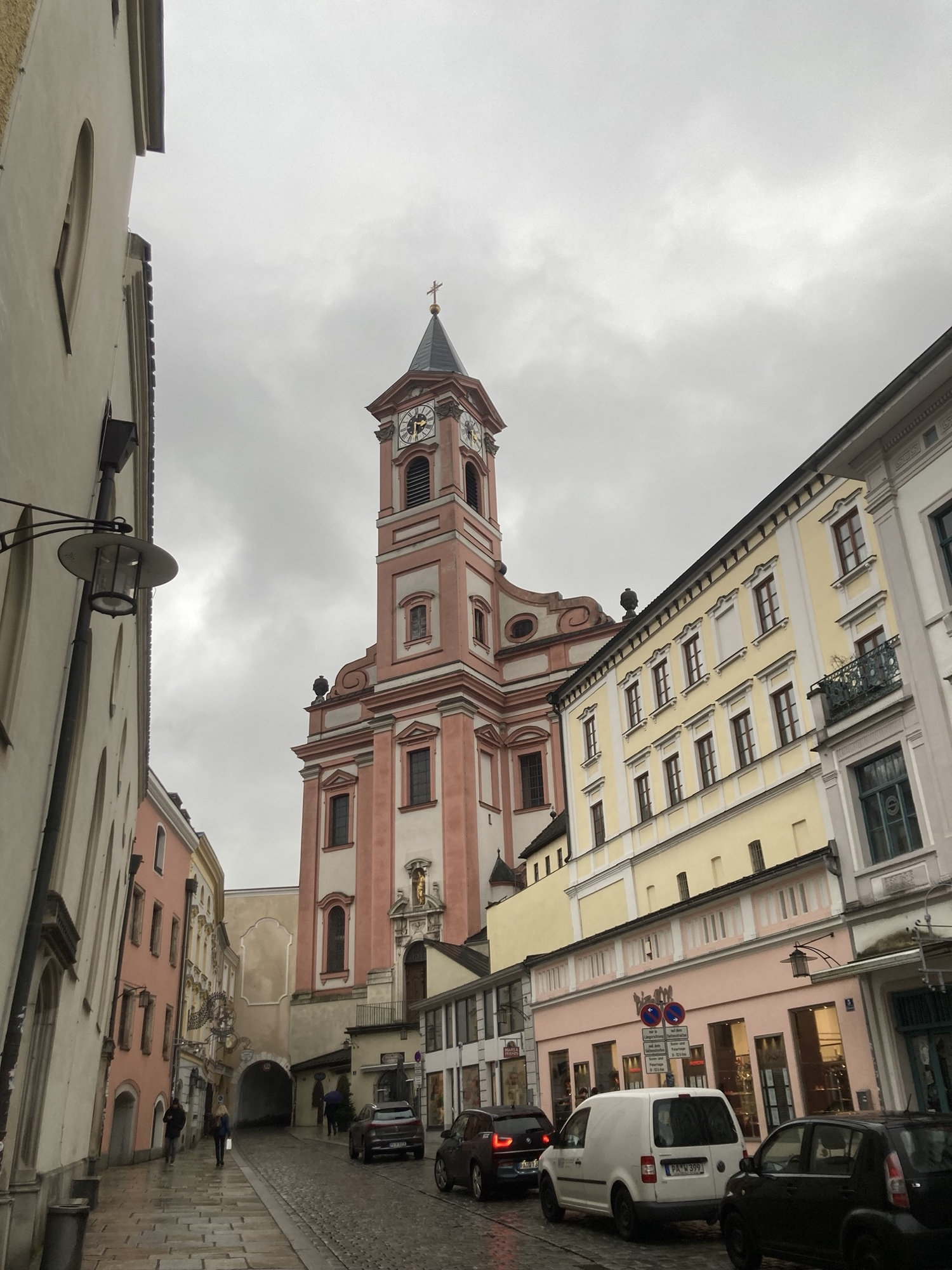 Stadtpfarrkirche St. Paul, ein schlankes Gebäude mit einem hohen Turm und roter Dekoration, links unten ist ein Stadttor der ehemaligen Befestigungsanlage zu sehen