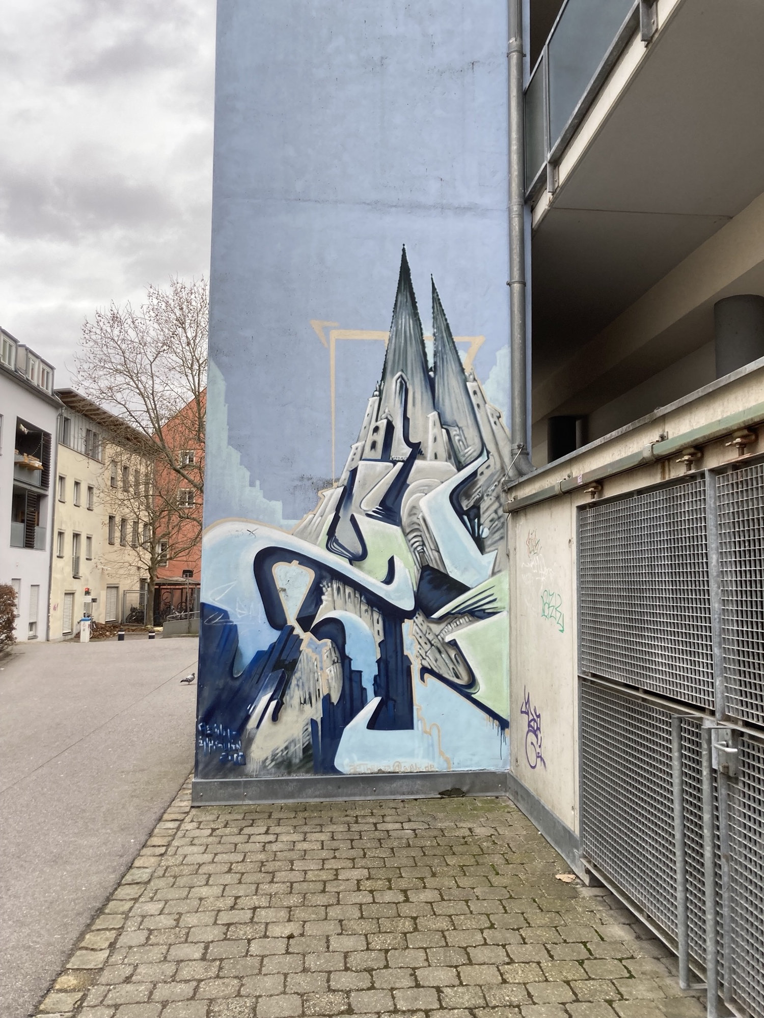 Graffiti an einer senkrechten Wand, zwei spitze Türme oben könnten die Türme des Doms darstellen, sie ragen in den Himmel und werden von blauen geschwungenen Streifen umwandelt, die Wege, Flüsse oder Wolken darstellen könnten