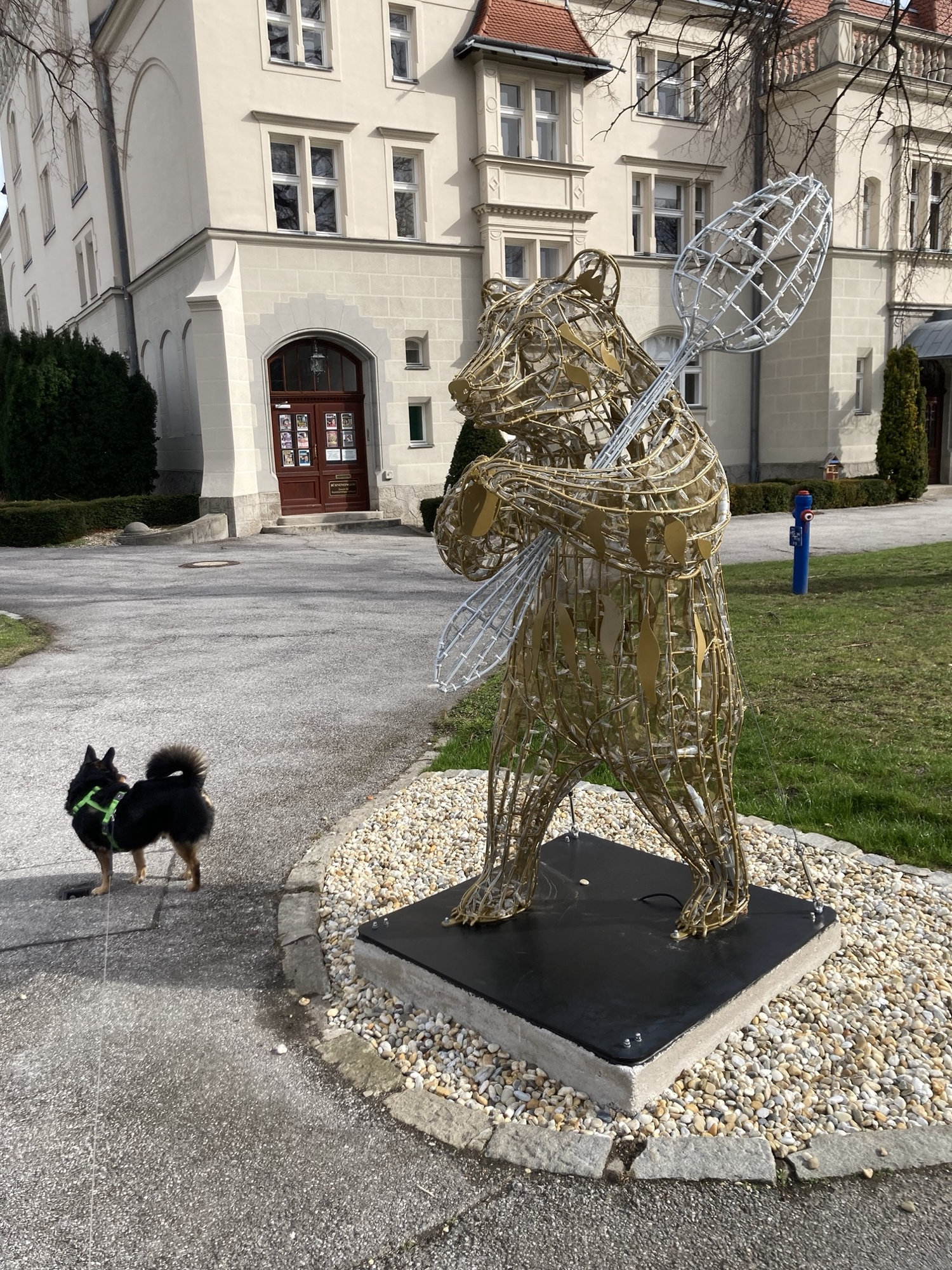 Metallstatue eines aufrecht stehenden Bären, der einen Löffel hält, daneben ein kleiner schwarzer Hund