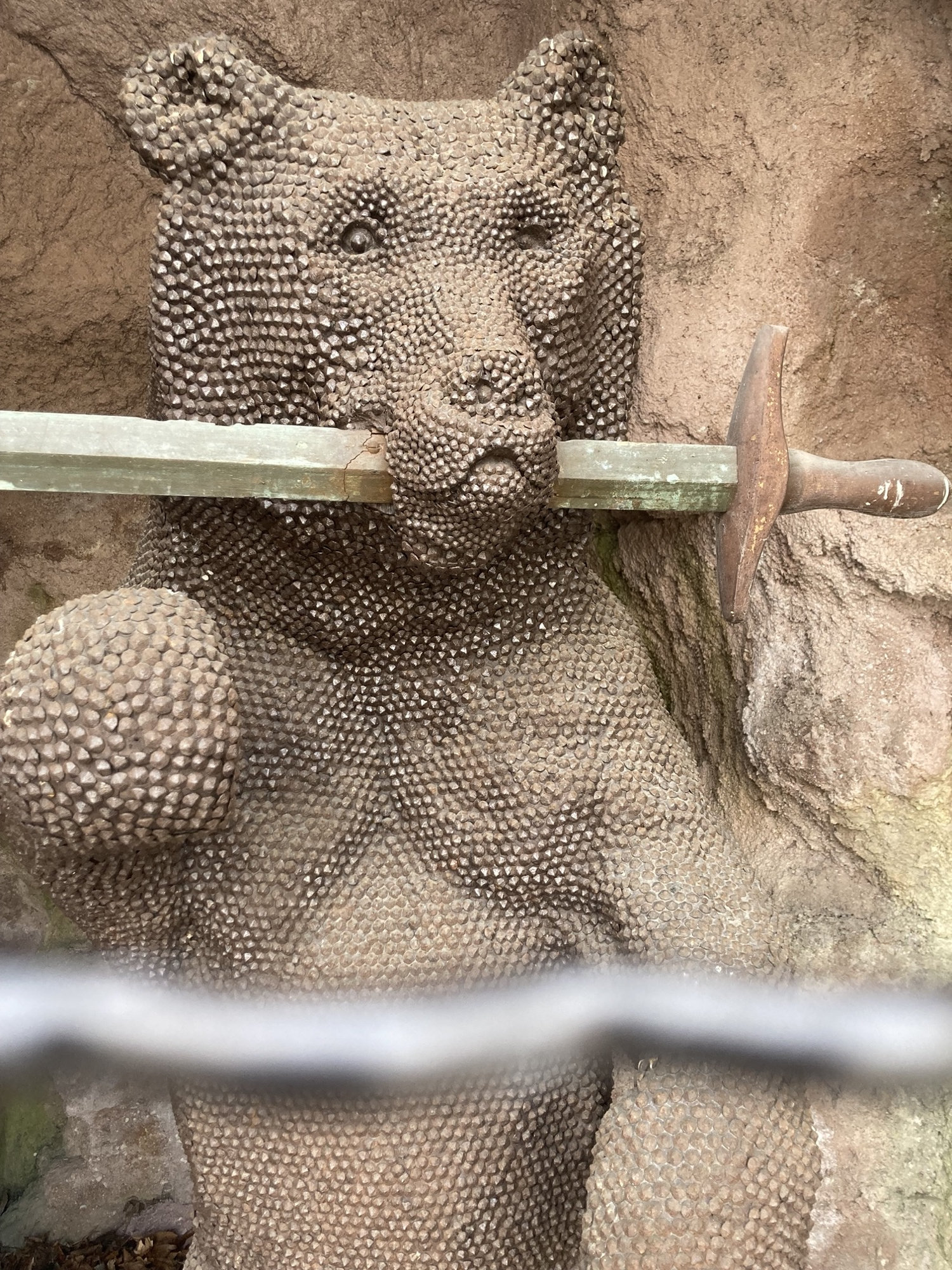 Statue eines aufrecht stehenden Bären, der ein Schwert im Maul hält