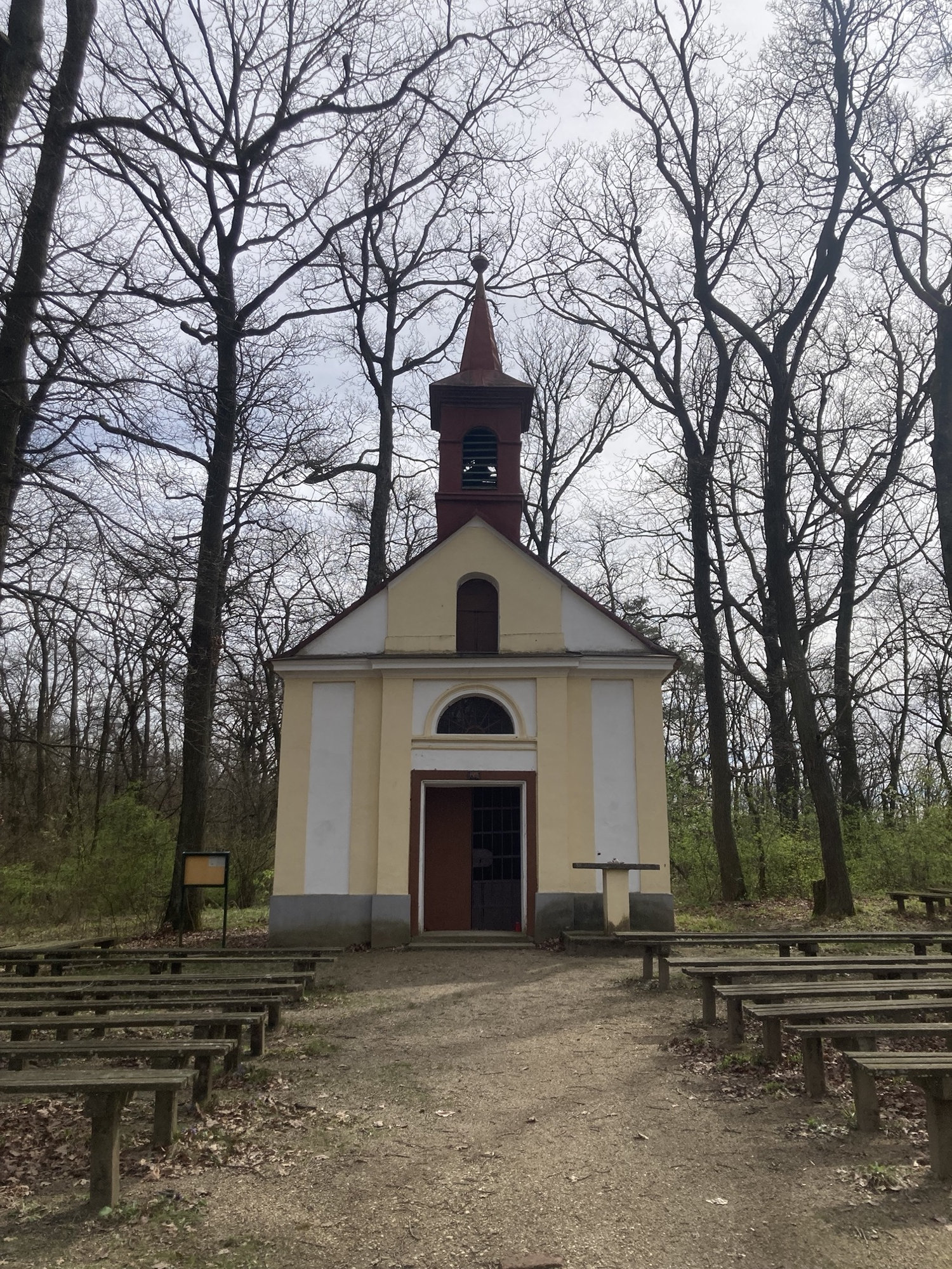 Wallfahrtskirche Klein Maria Dreieichen, ein gelbes Gebäude mit einem braunen Turm, davor stehen links und rechts Holzbänke