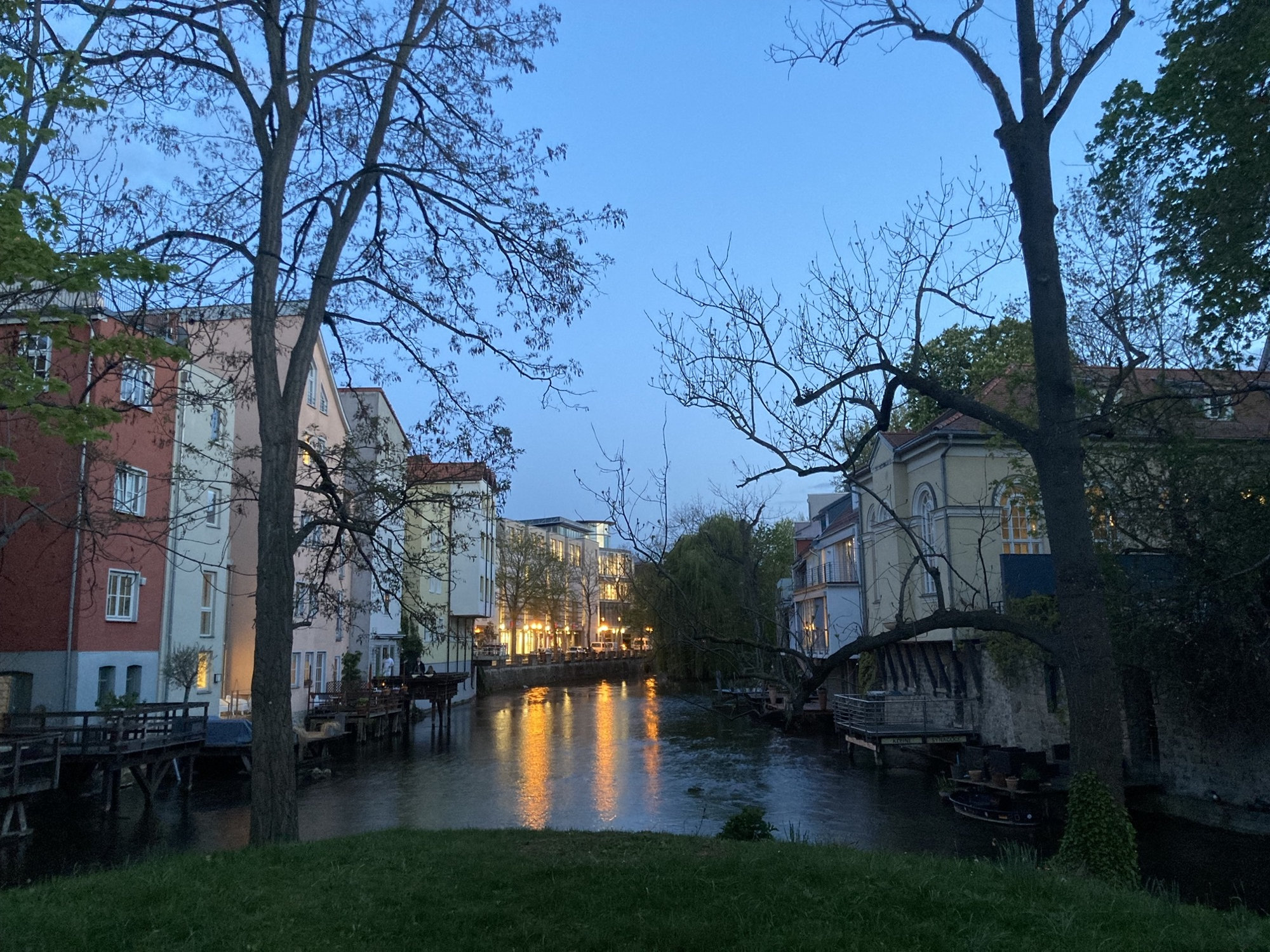 abendlicher Ausblick über die Wilde Gera, links und rechts Bäume, im Hintergrund beleuchtete Häuser an der Promenade