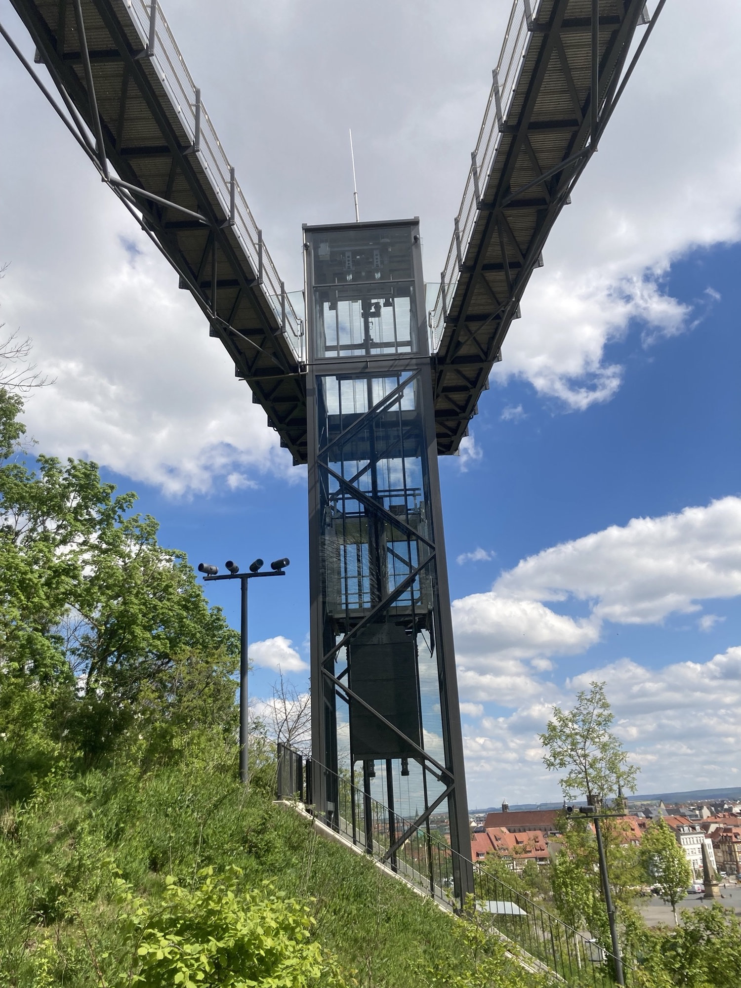 Glasaufzug auf den Petersberg, in der Mitte führt der Glasaufzug nach oben, vom oberen Ausgang des Aufzugs ragen zwei Gänge oben aus dem Bild raus, die Kombination bildet die Form eines V