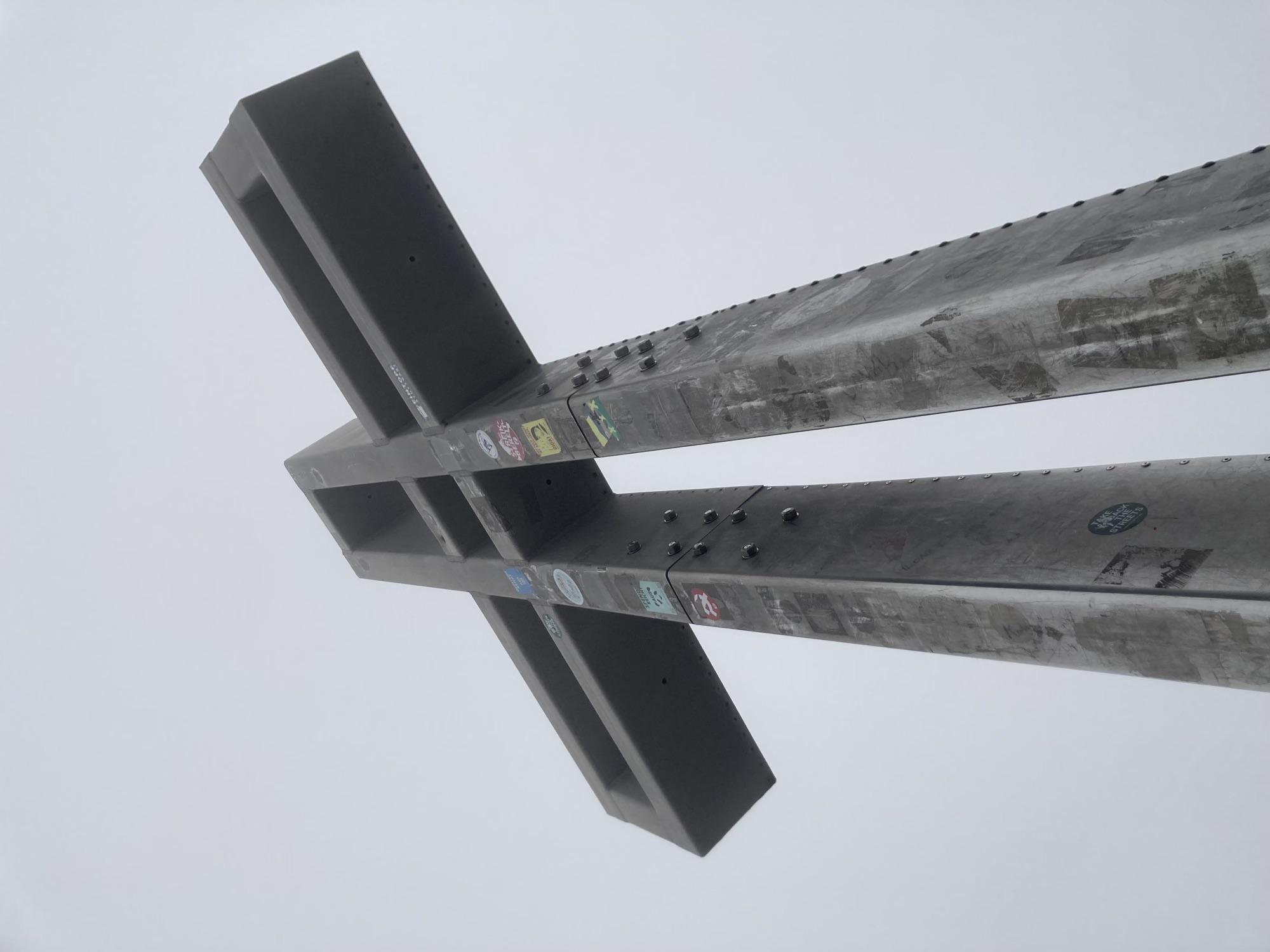 Gipfelkreuz am Schneeberg im Fokus, ein Metallkreuz mit Nieten zusammengeschraubt, Sticker in verschiedenen Verwitterungszuständen auf dem Kreuz