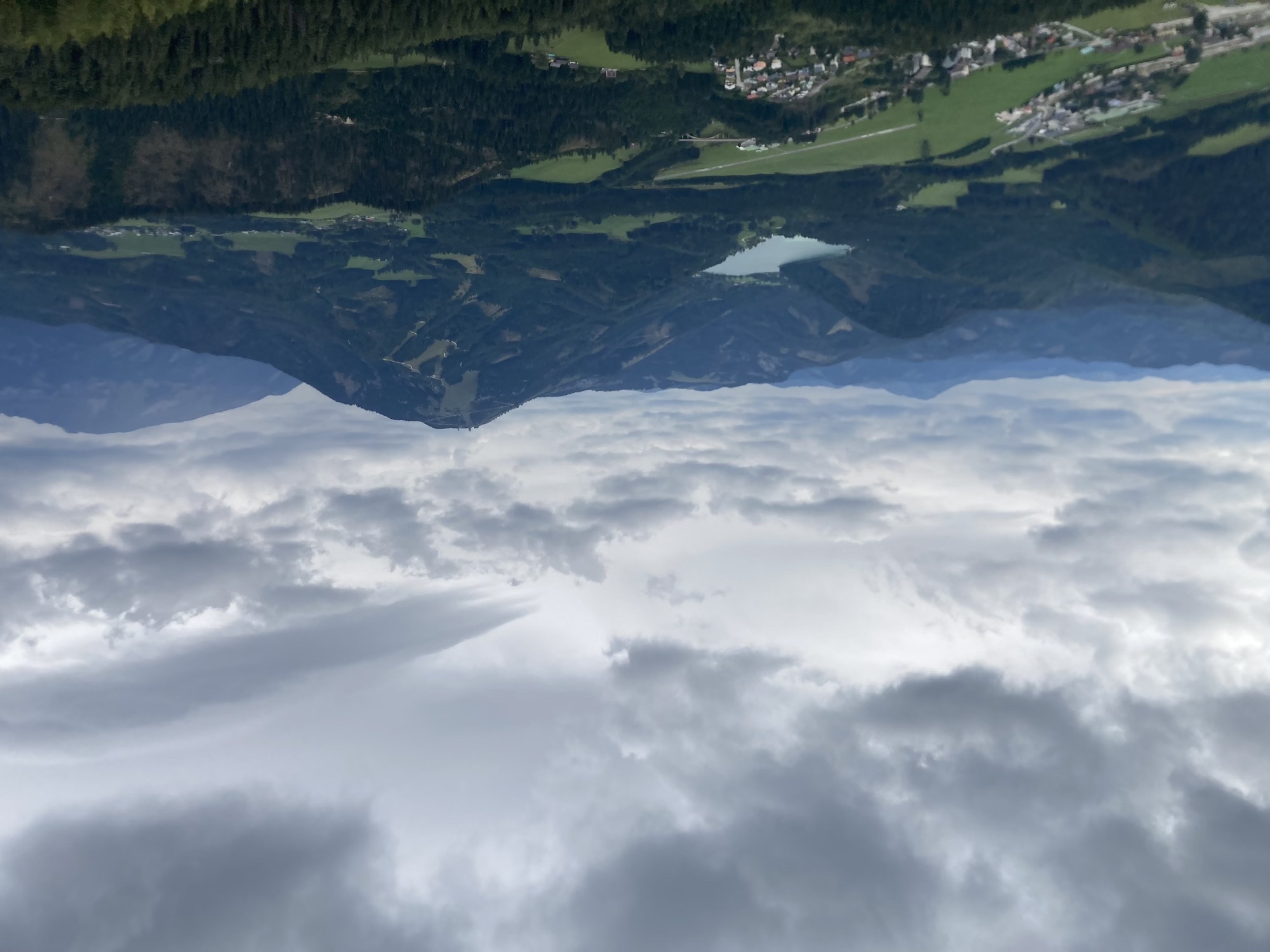 Ausblick vom Aussichtsturm, bewaldete Berge, in der Mitte ein See, dahinter düster bewölkter Himmel