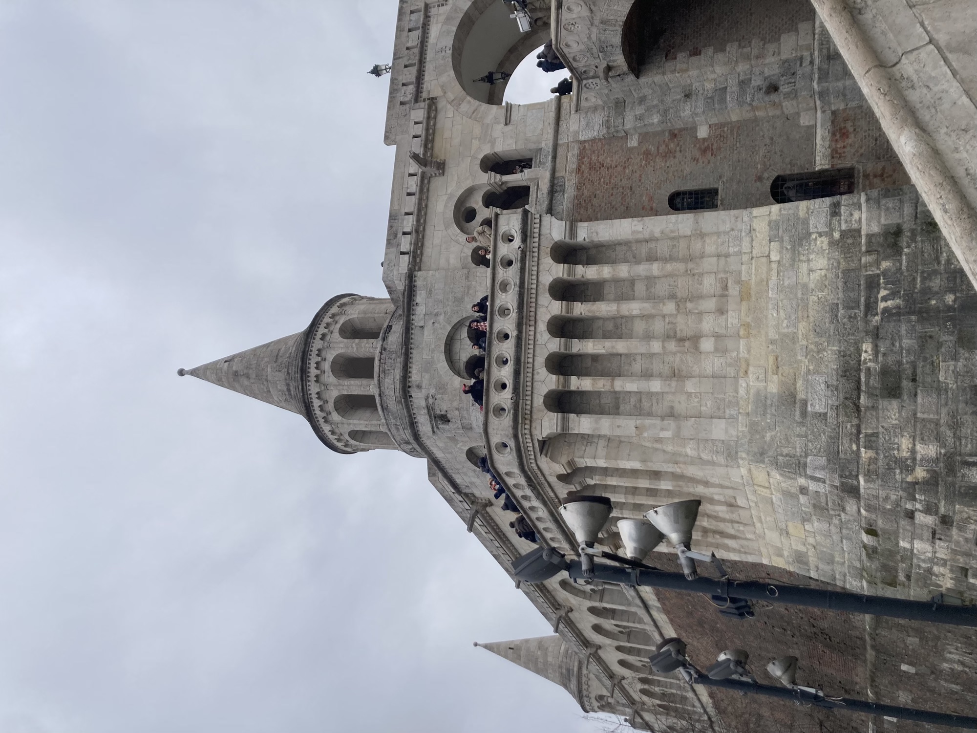 Burgmauer mit einer von Säulen geschützten Balustrade, auf der Tourist:innen die Aussicht genießen und fotografieren, darüber ein runder Turm mit einem spitzen Dach